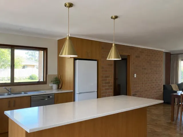 Kitchen with two brass pendant lights over a large island, brick wall and timber cabinets in Mount Hutton